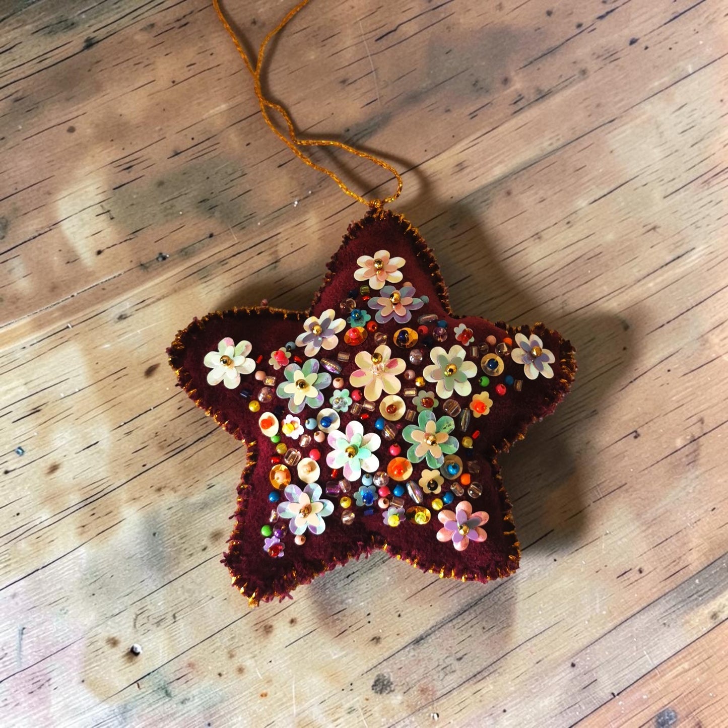 Étoile de Noël Thalie's Factory en velours bordeaux, ornée de fleurs et perles multicolores cousues à la main.